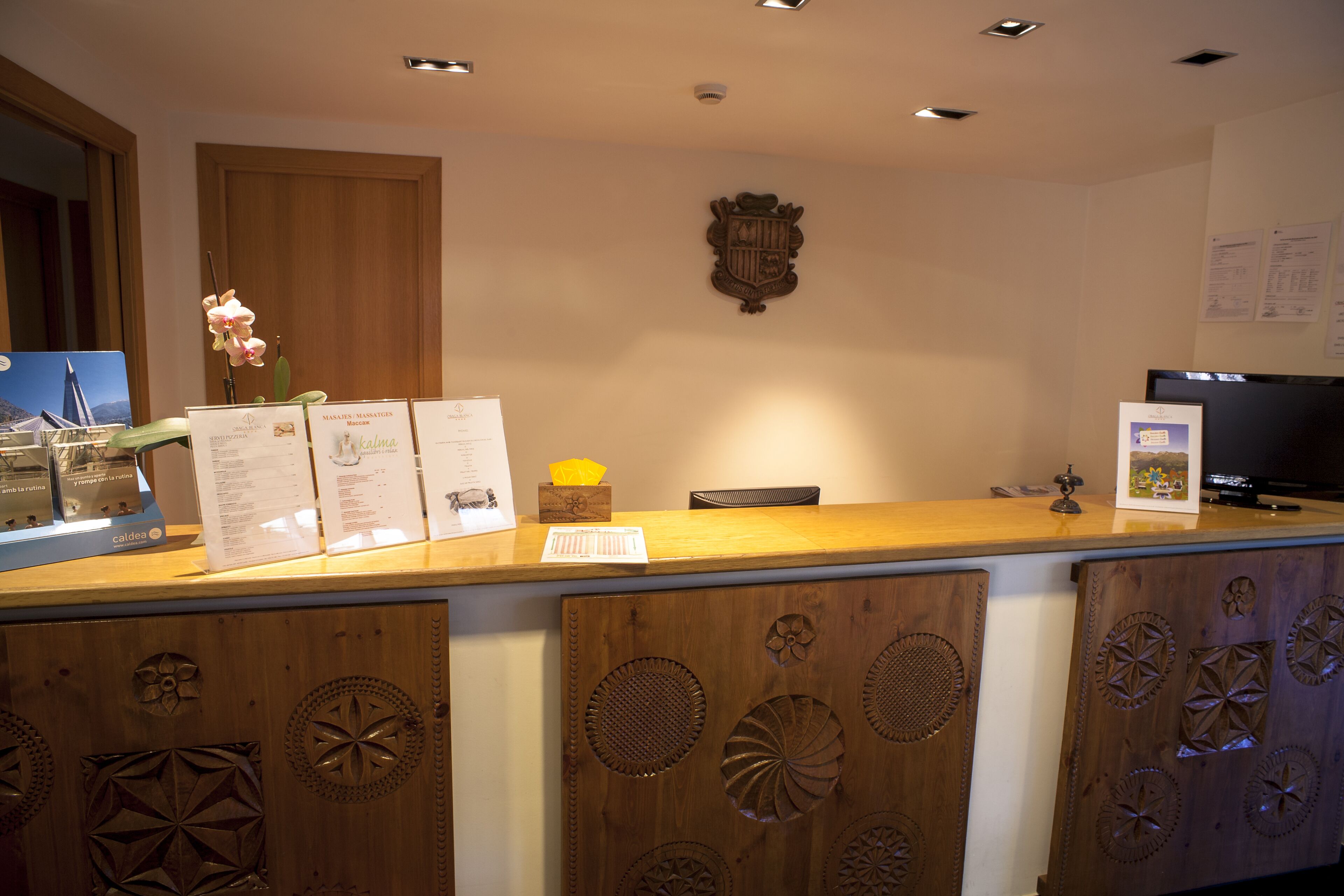 A reception desk with a wooden finish, a mounted coat of arms, and a television screen.