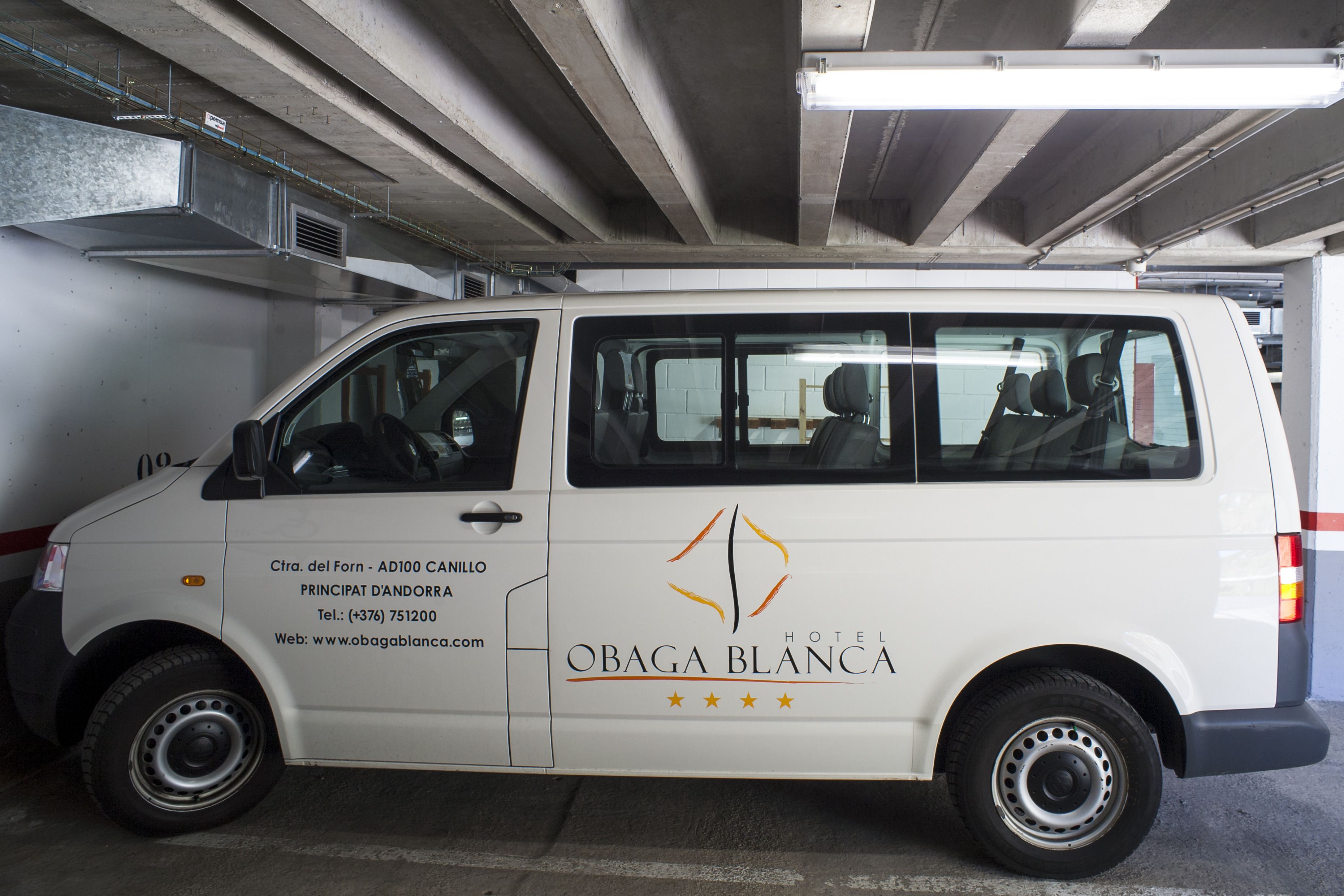 Una furgoneta blanca con el logotipo y la información de contacto del hotel OBAGA BLANCA estacionada en un garaje.