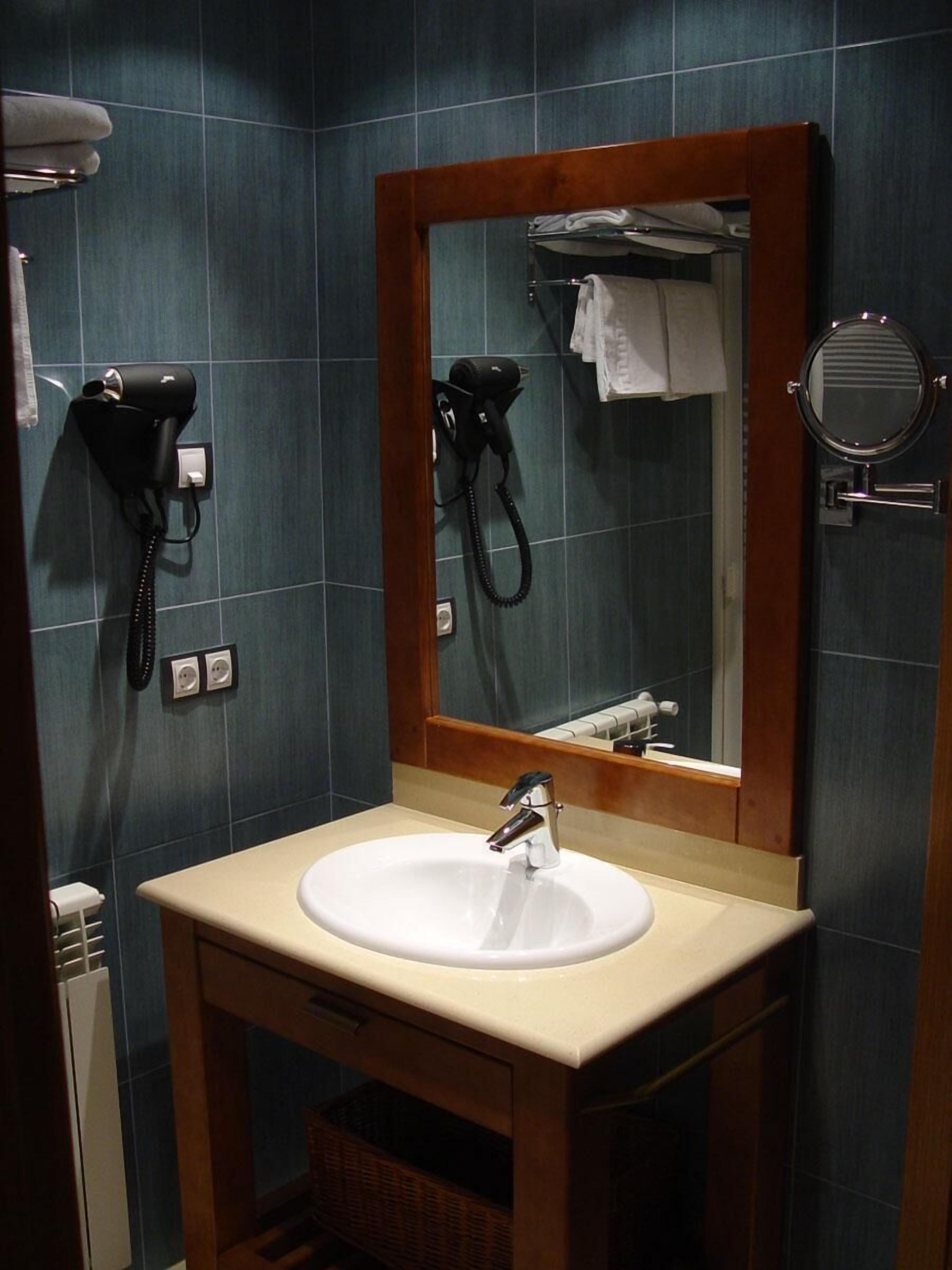 Casa de banho com lavatório, espelho, secador de cabelo e porta-toalhas.