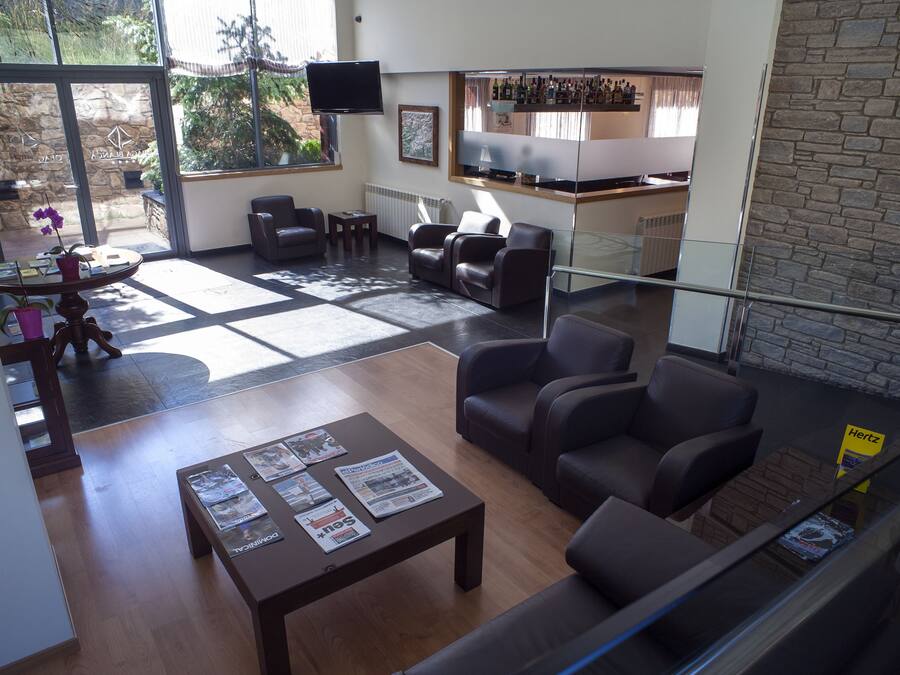 A modern living room with leather sofas, a coffee table with magazines, a stone wall, and a kitchen area with a bar.