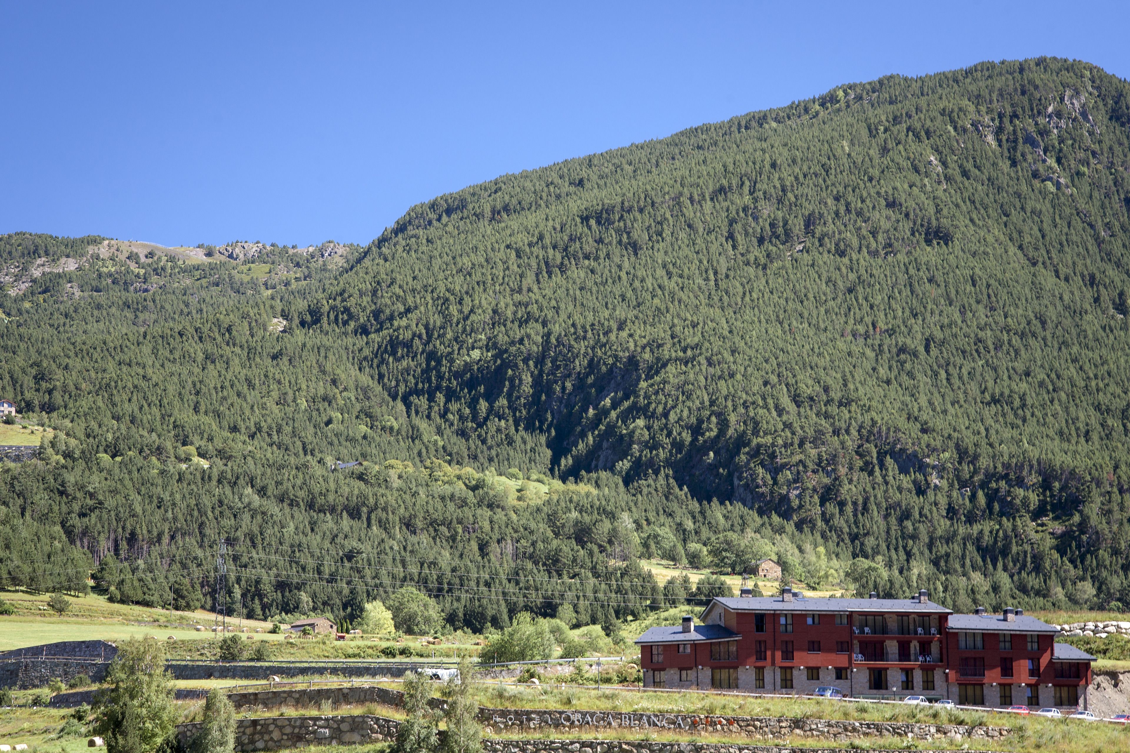 Een rood gebouw met meerdere verdiepingen en balkons, gelegen in een bergachtig landschap met dicht bos.