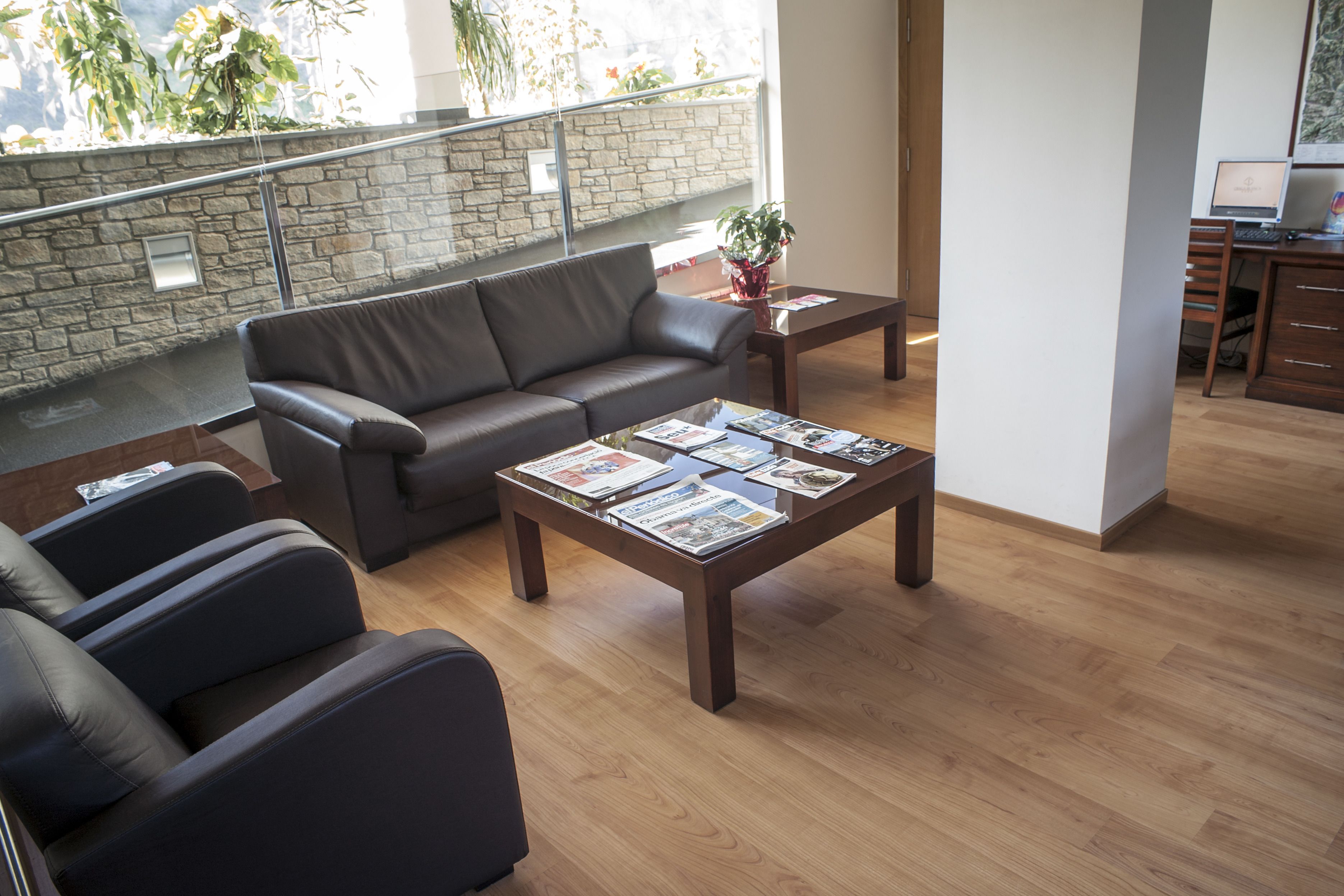 A modern living room with a leather sofa, a wooden coffee table with magazines, and a stone wall with a balcony.