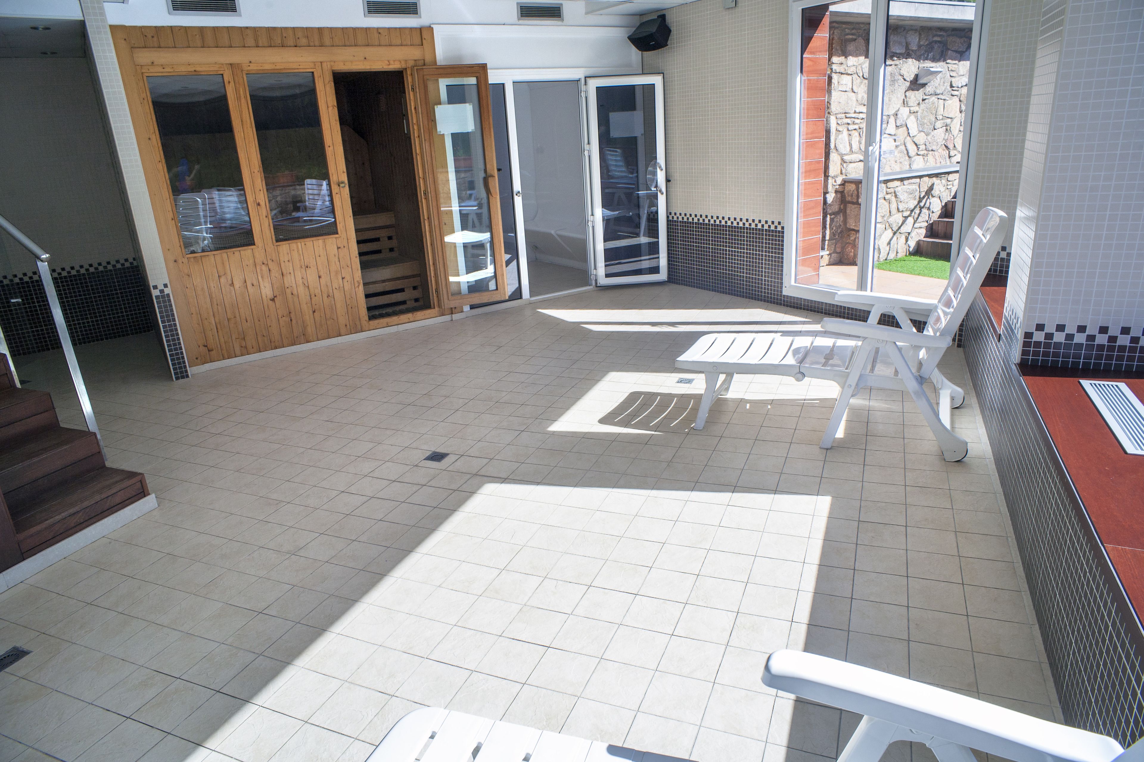 A tiled patio area with a white lounge chair, a wooden door, and a stone wall.
