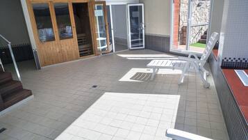 A tiled patio area with a white lounge chair, a wooden door, and a stone wall.