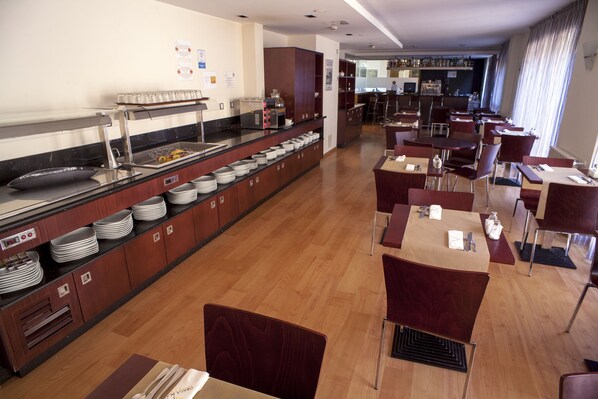 A hotel restaurant with a buffet area, multiple dining tables, and chairs.
