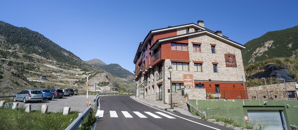 A hotel with a stone facade, multiple balconies, and a clear view of the surrounding mountains.