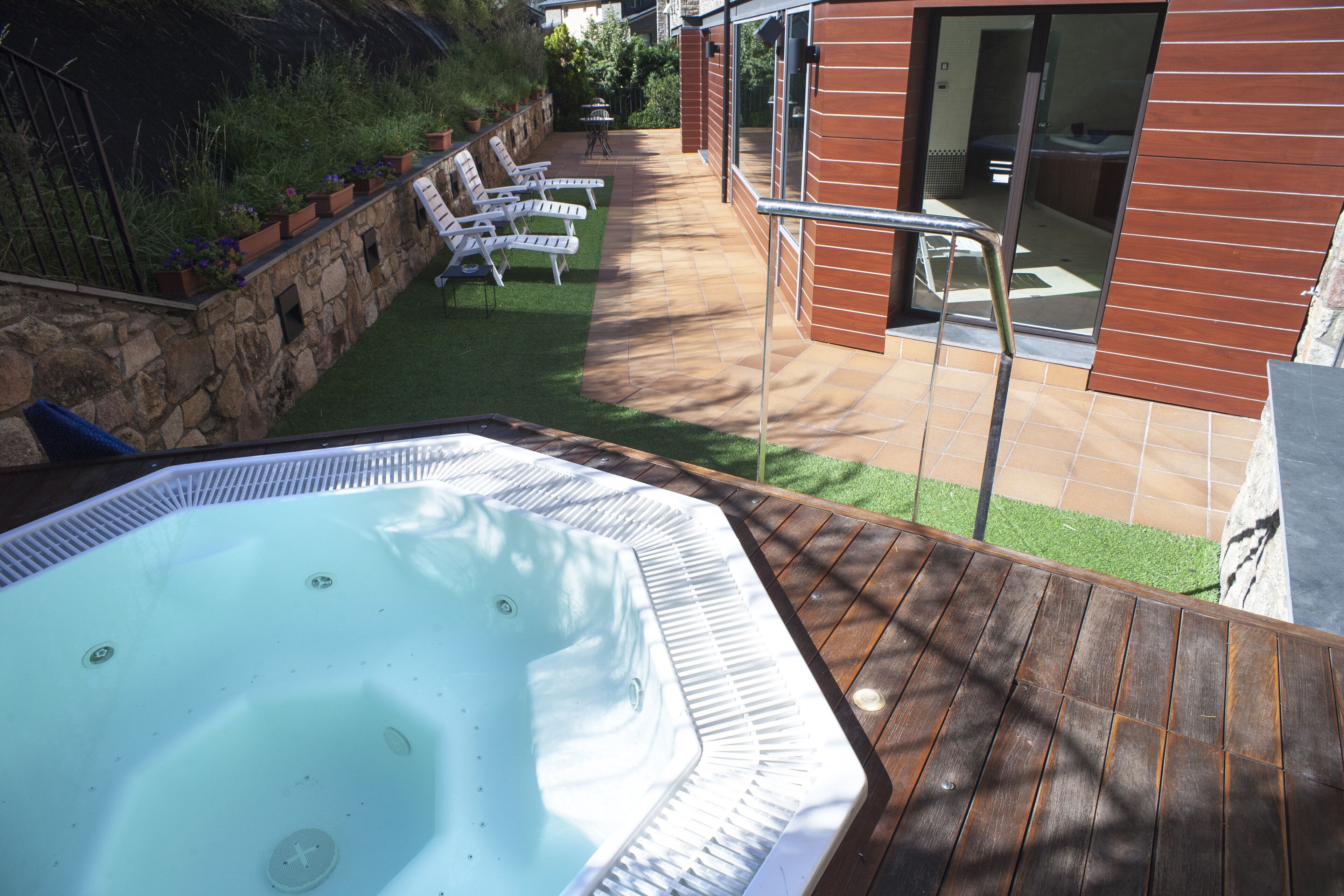 Een hottub op een houten terras, met een stenen muur en plantenbakken.
