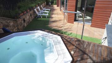 Een hottub op een houten terras, met een stenen muur en plantenbakken.