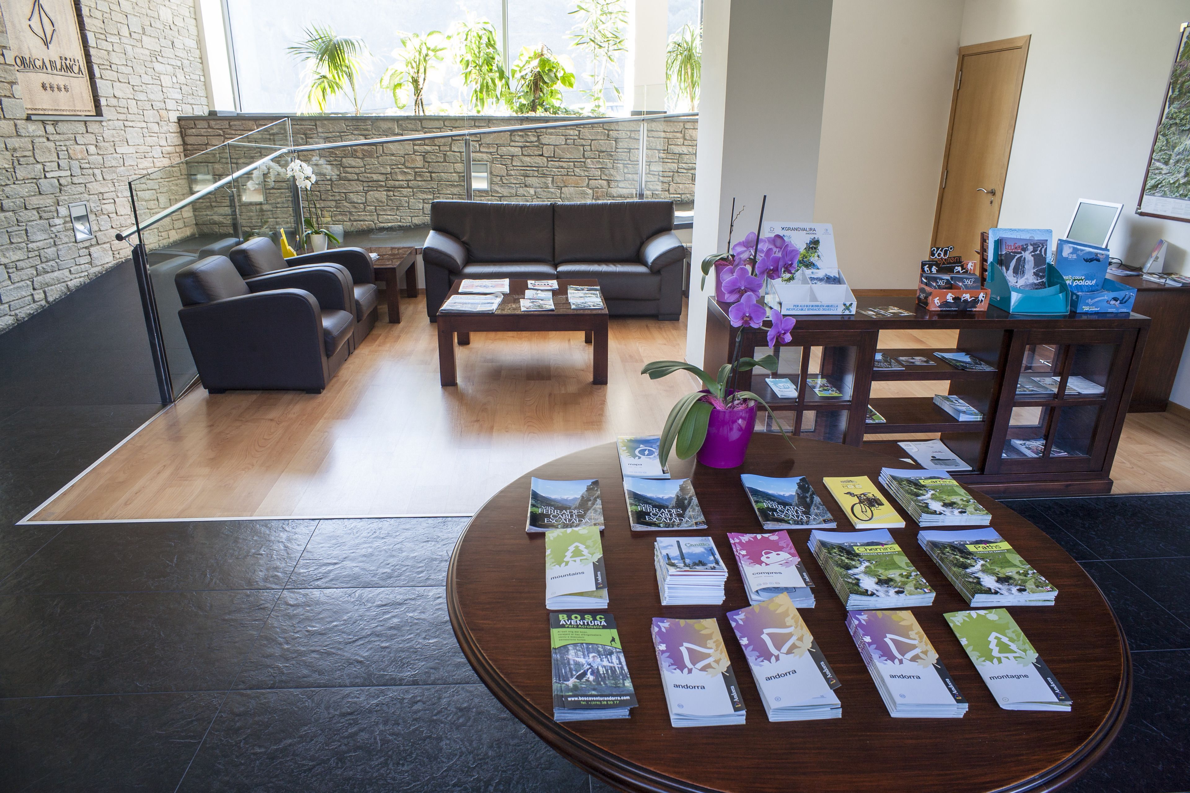 A modern lobby with a stone wall, leather sofas, a wooden coffee table, and a display of brochures.