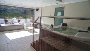 A spa area with a hot tub, wooden steps, and a view of greenery through a large window. - Hotel Obaga Blanca (Canillo)