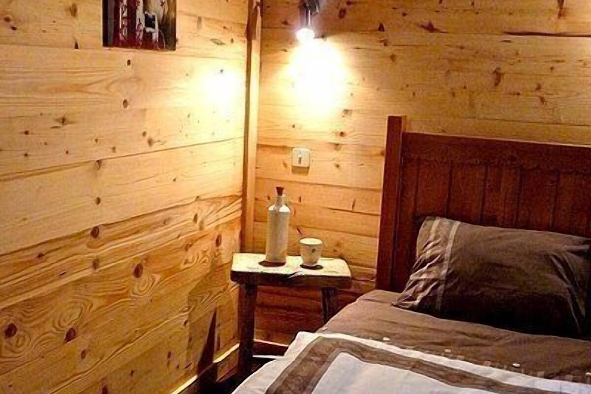 Een houten kamer met een bed, een nachtkastje met lamp en een wandplank.