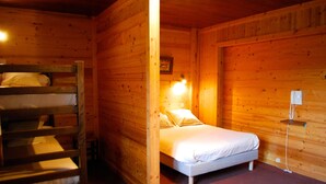 Een houten kamer met een stapelbed, een enkel bed en een wandlamp.