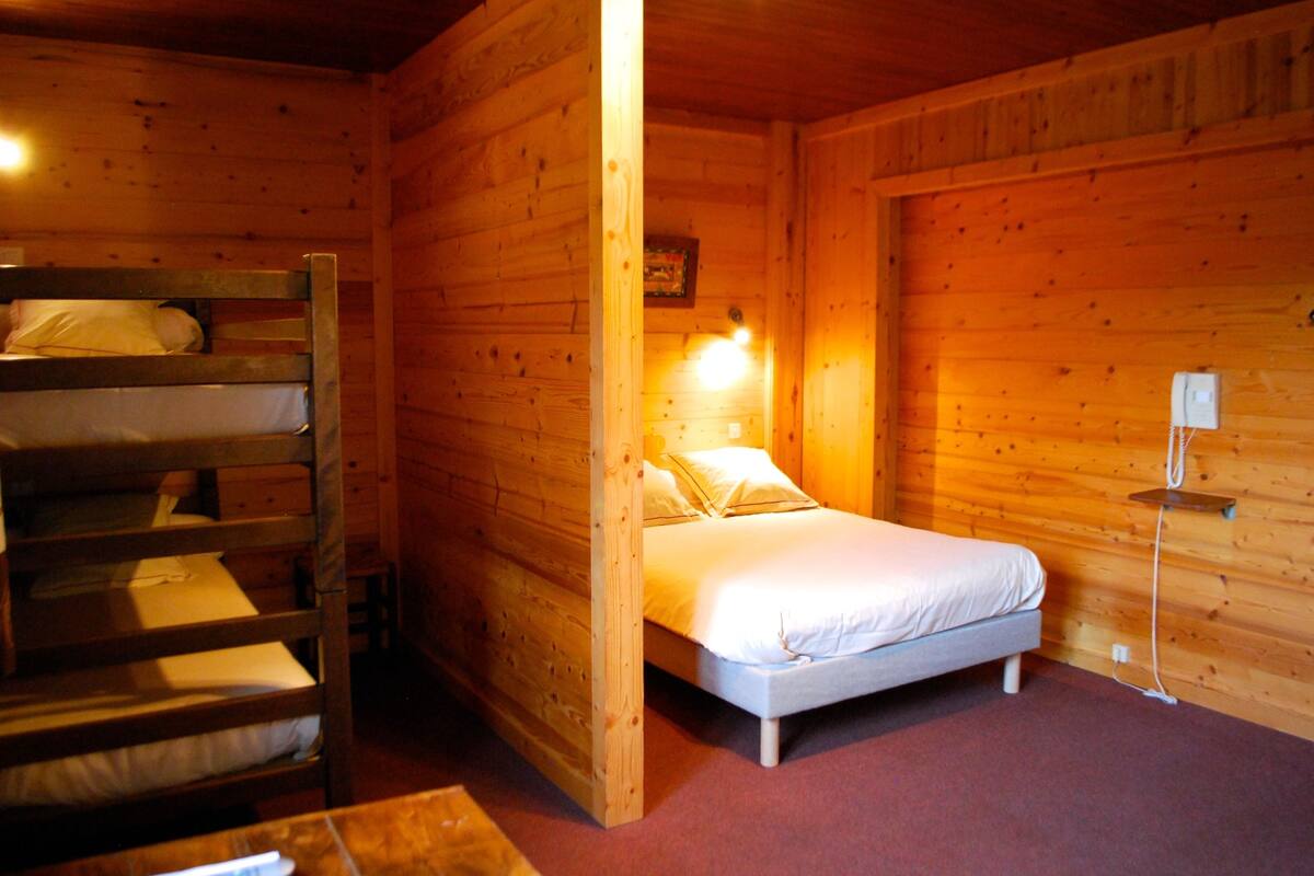 Een houten kamer met een stapelbed, een enkel bed en een wandlamp.