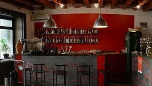 Zona de bar con paredes rojas, luces colgantes y una variedad de botellas y copas.