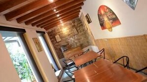 Interior de restaurante con vigas de madera en el techo, paredes de piedra y zona de comedor con mesas y sillas.