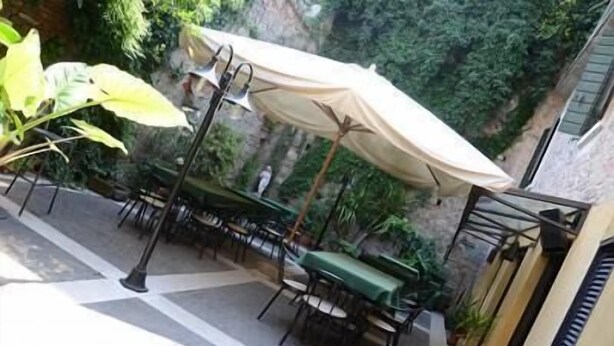Un patio al aire libre con mesas y sillas, un paraguas grande y vistas a un área verde exuberante.