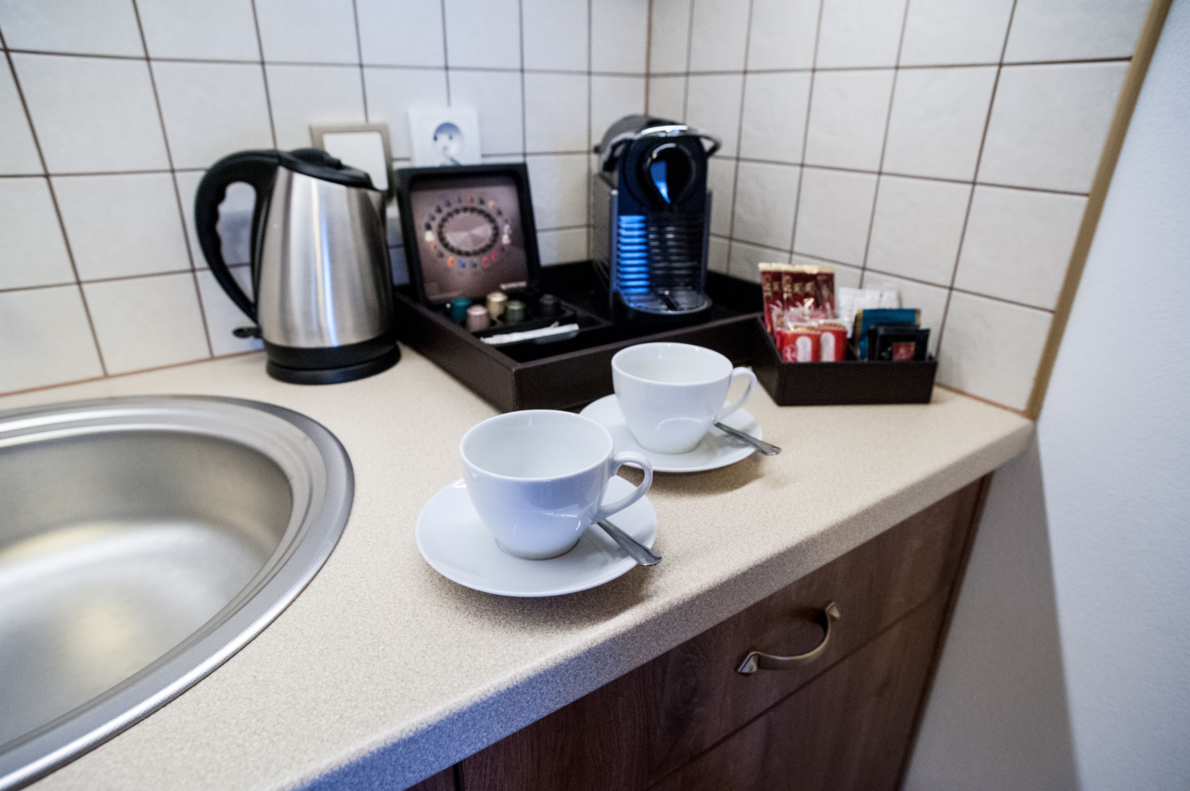 Una encimera de cocina con una cafetera, dos tazas blancas, un hervidor y una caja de pañuelos.
