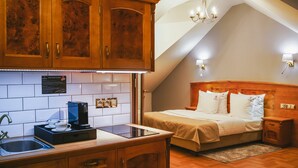 A hotel room with a kitchenette, a bed with a wooden headboard, a nightstand, and a chandelier.