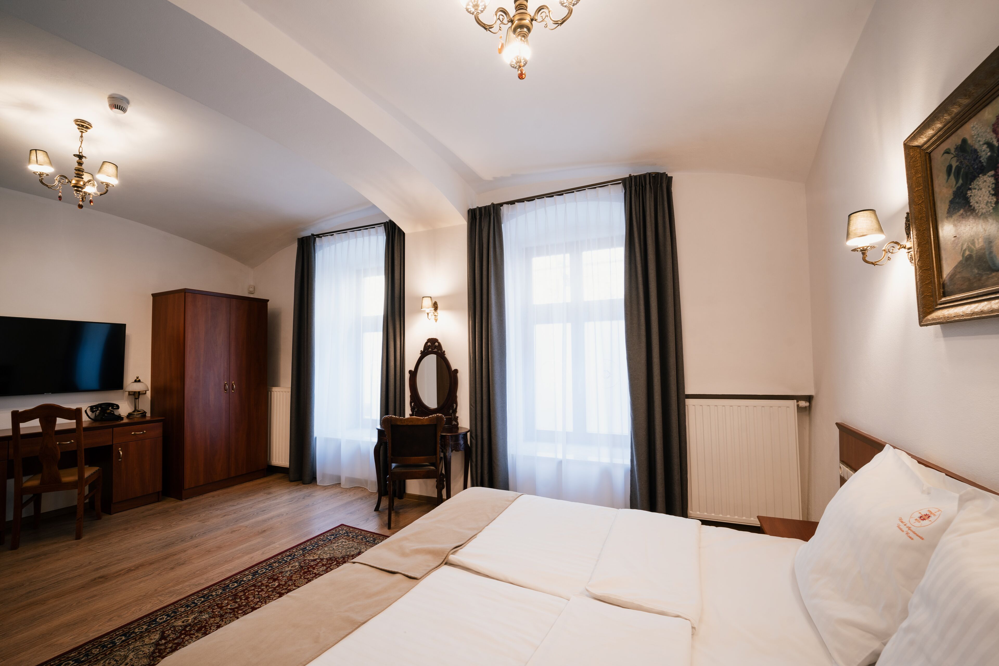 A hotel room with a large bed, a desk with a chair, a television, a wardrobe, and a painting on the wall.
