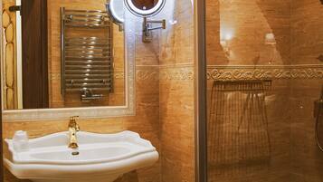 A bathroom with a pedestal sink, a mirror with a light, a glass shower enclosure, and a towel rack.