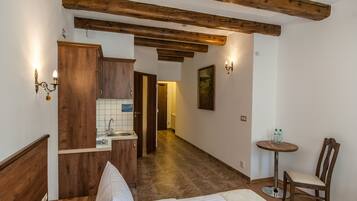 Habitación de hotel con cama de madera, una pequeña kitchenette, una silla de madera y una mesa redonda con dos botellas.