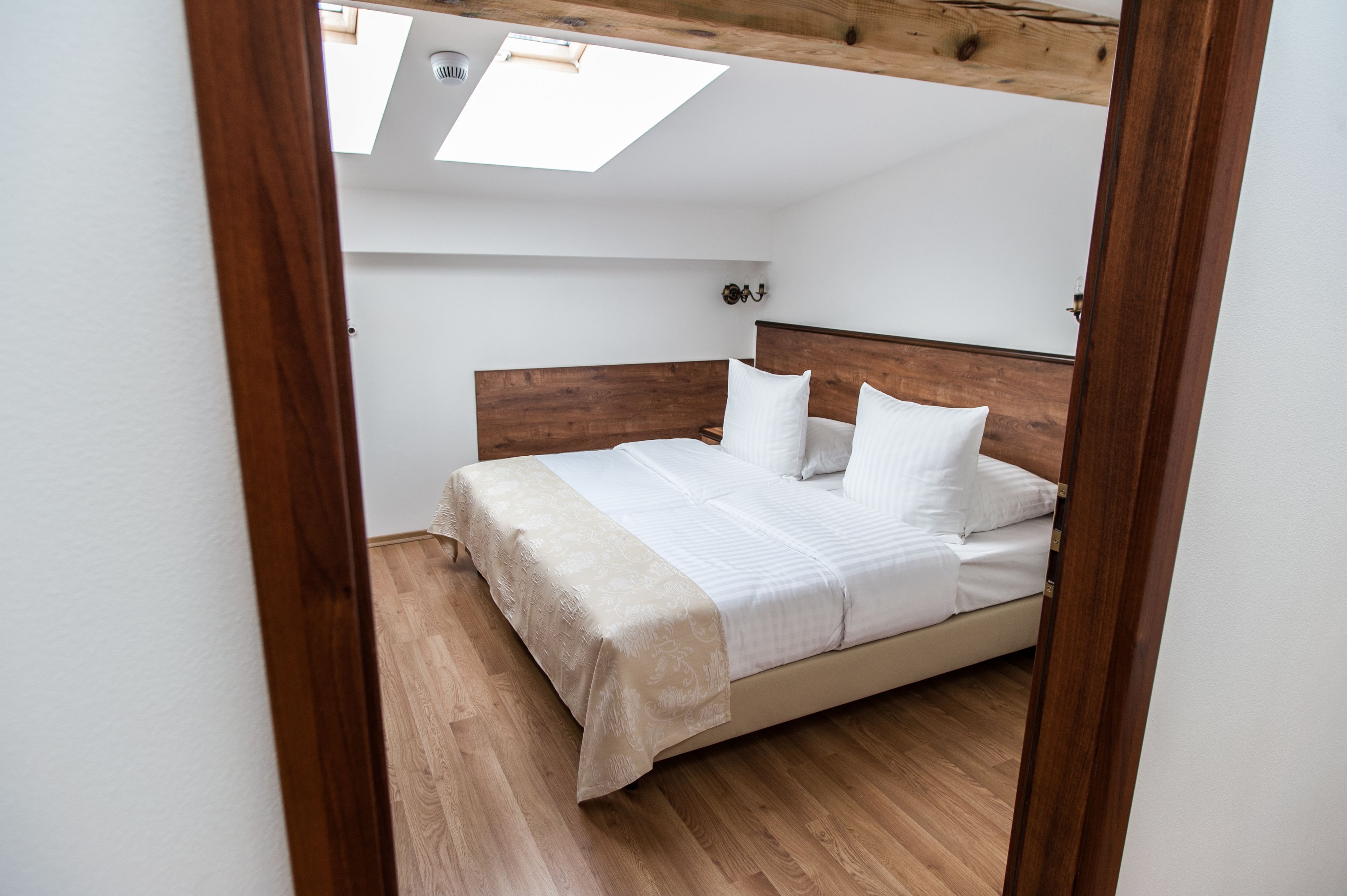 Un dormitorio con cabecera de madera, cama con ropa blanca y tragaluz.