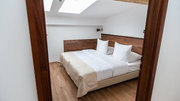 Un dormitorio con cabecera de madera, cama con ropa blanca y tragaluz.