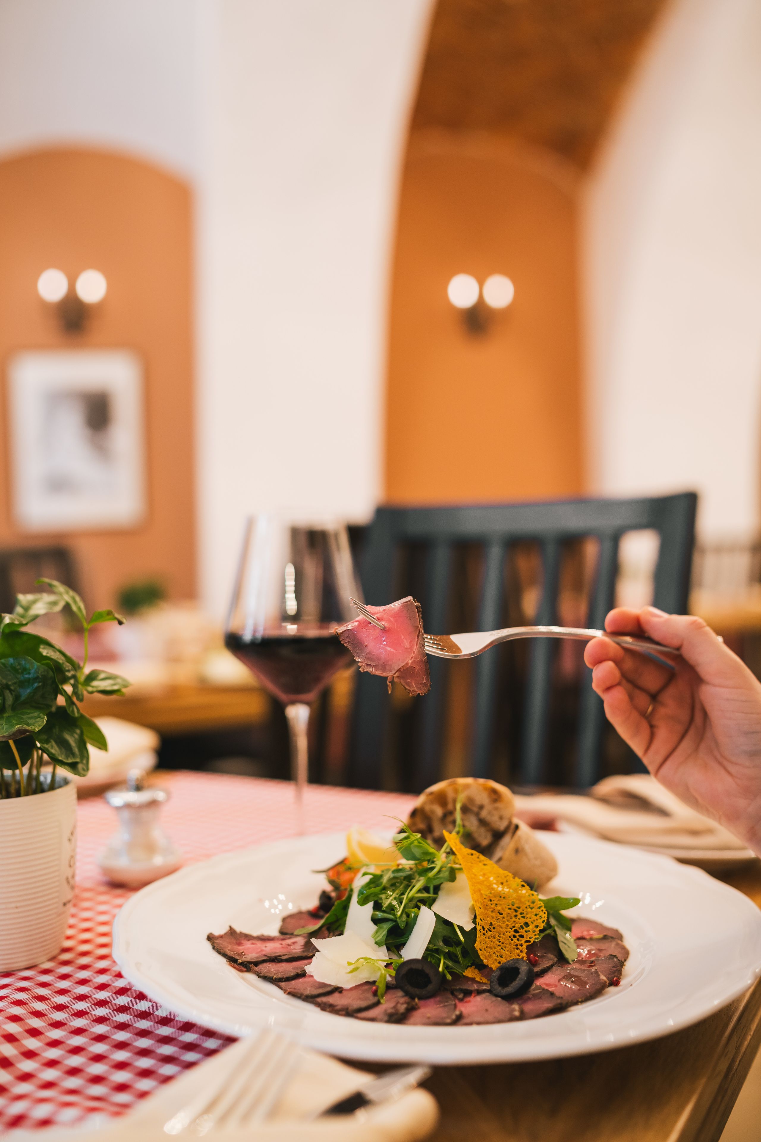 A dining table with a plate of steak and vegetables, a glass of red wine, and a fork.