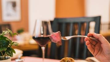 A dining table with a plate of steak and vegetables, a glass of red wine, and a fork.