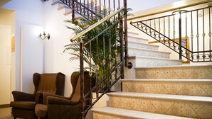 A staircase with a metal railing, carpeted stairs, and a brown armchair in a room with a white wall and a plant.