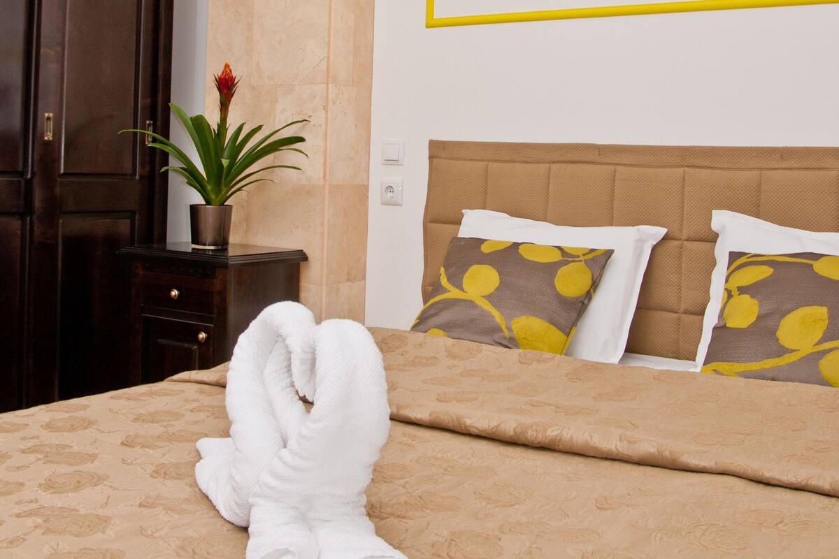 A neatly made bed with a brown headboard, two pillows with a yellow leaf pattern, and a white towel on the bed.