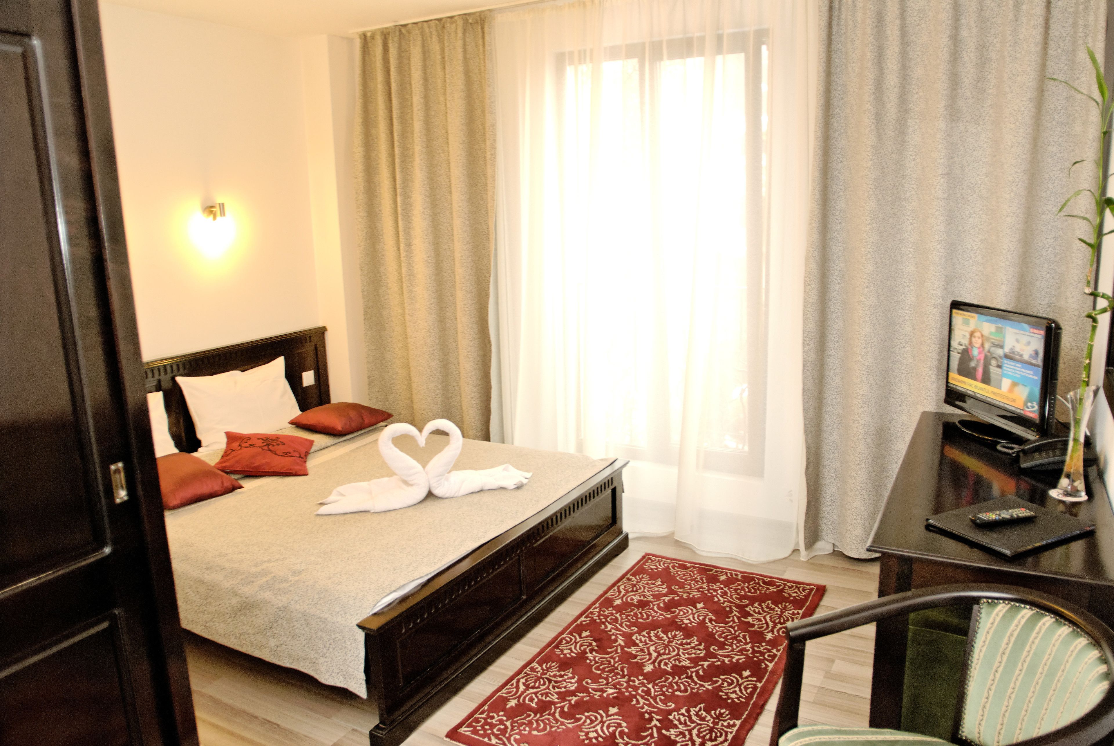Ein Hotelzimmer mit Bett, Schreibtisch, Computer, Stuhl und einem Fenster mit Vorhängen.