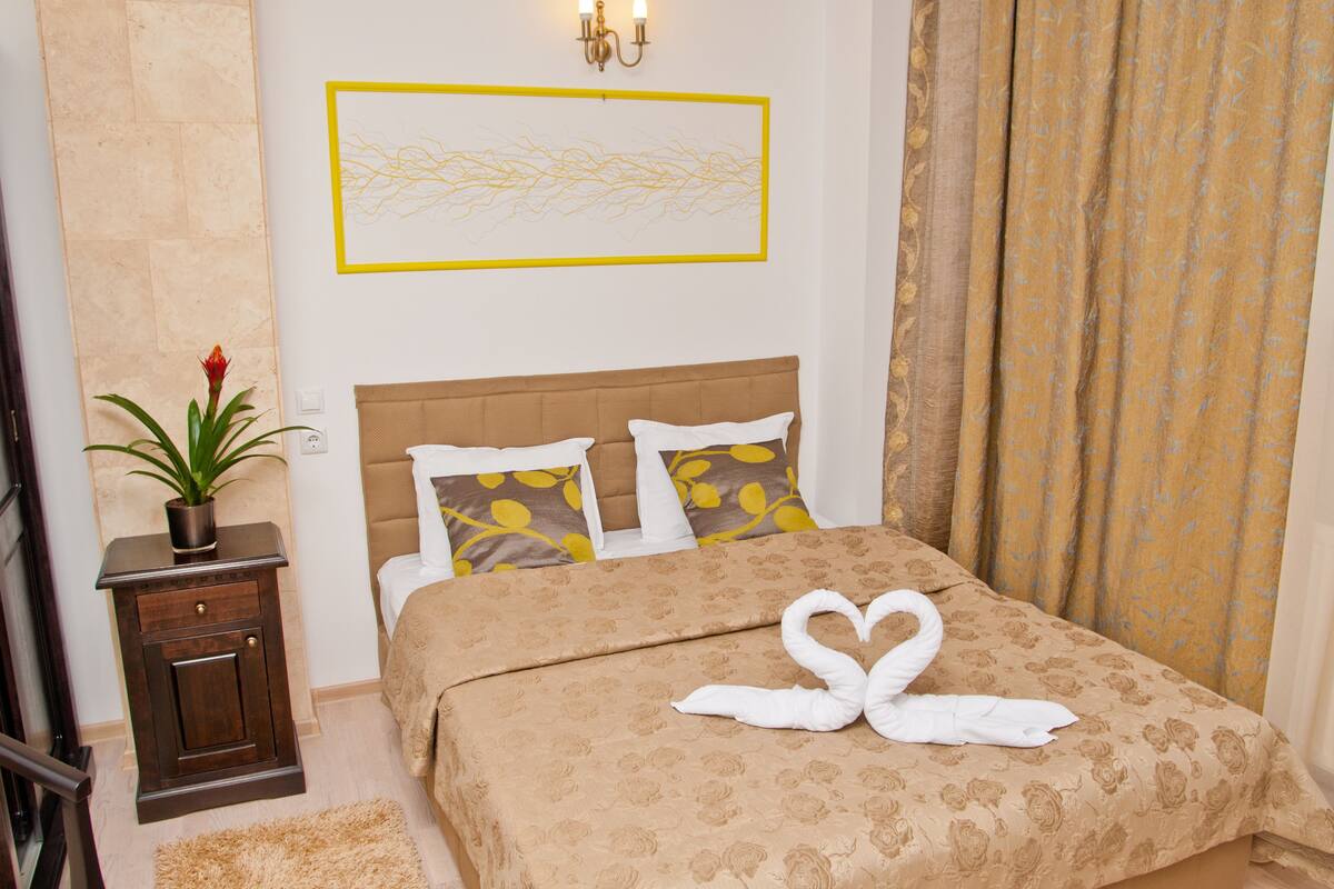 A neatly arranged bedroom with a bed, pillows, a bedside table with a plant, and a wall-mounted artwork.