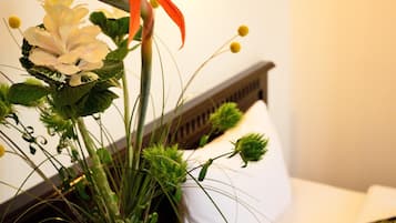 A close-up of a floral arrangement with a variety of flowers and greenery, placed on a surface with a white pillow and a wooden headboard in the background.