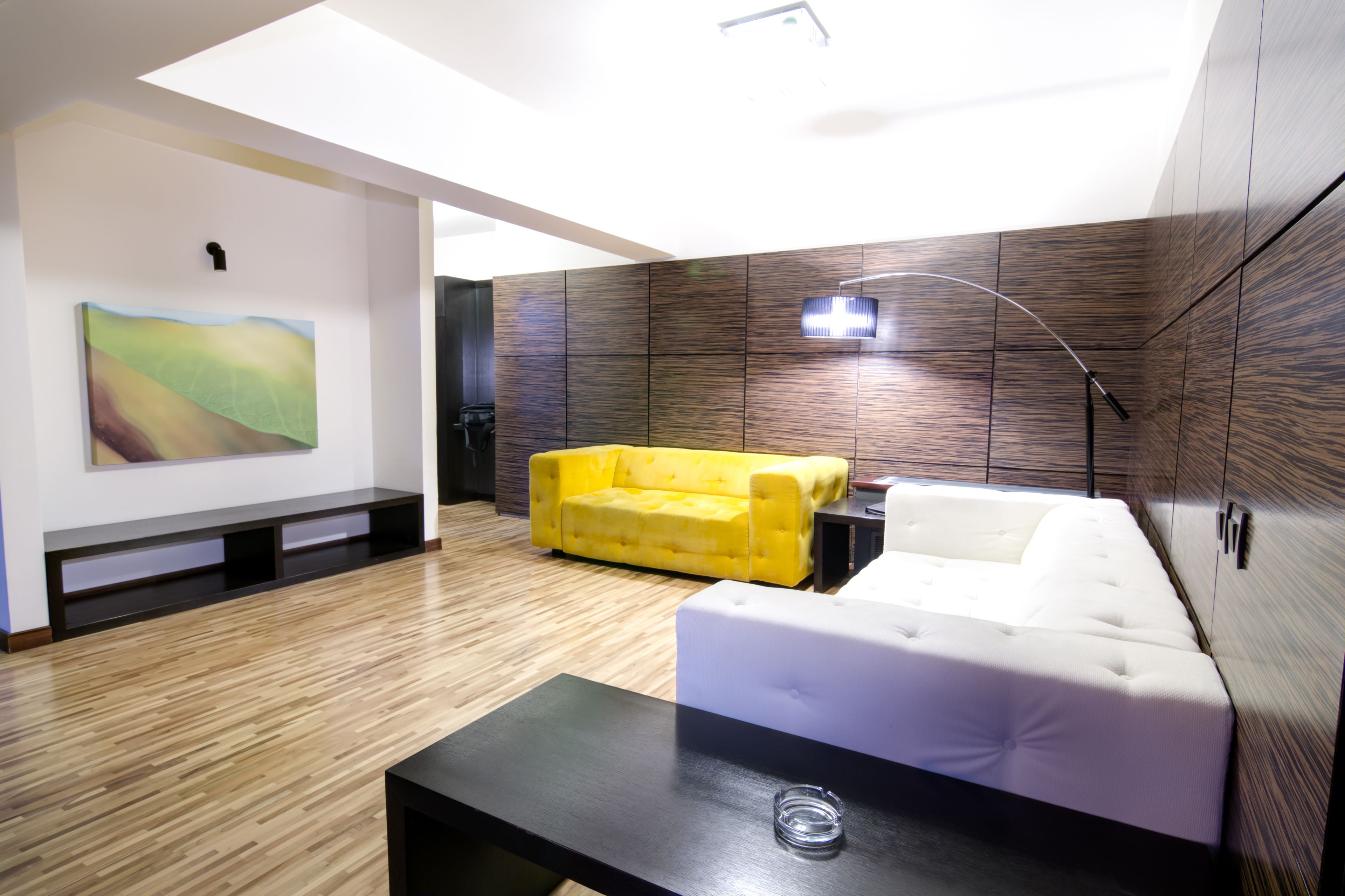 A modern living room with a yellow sofa, white sofa, and a black coffee table.