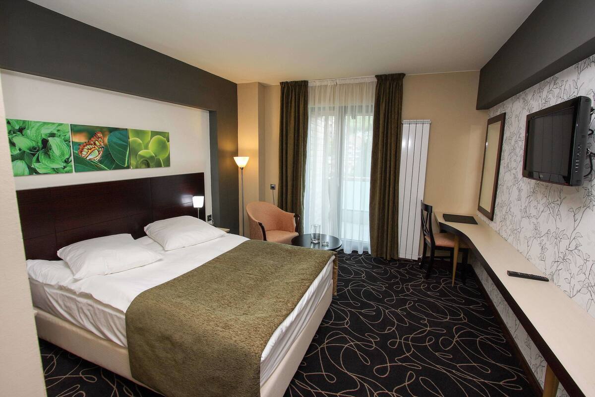 Ein Hotelzimmer mit einem Bett, einem Schreibtisch, einem Stuhl, einem Fernseher und Bildern an der Wand.