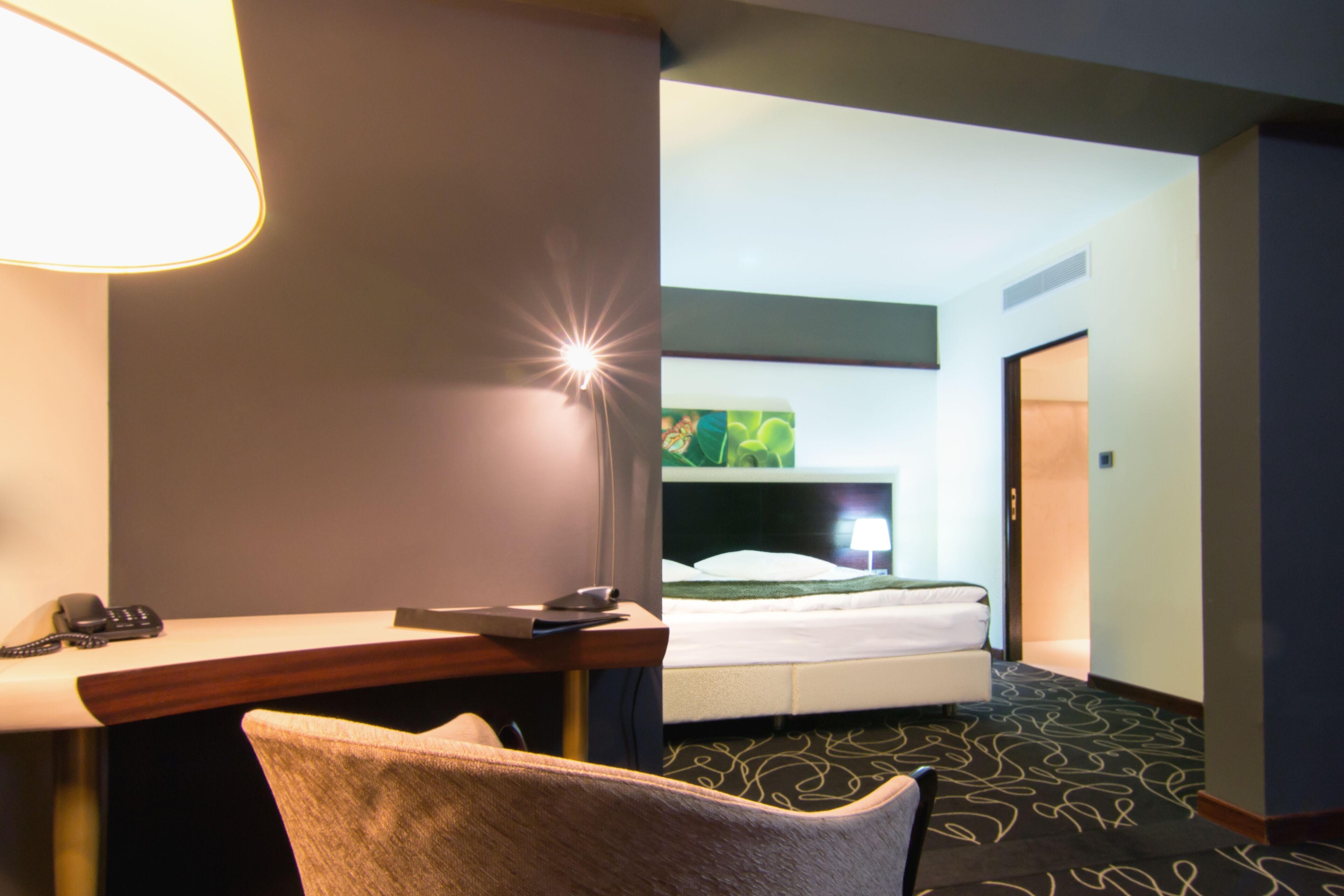 A hotel room with a desk, chair, bed, and a view of a green landscape through the window.
