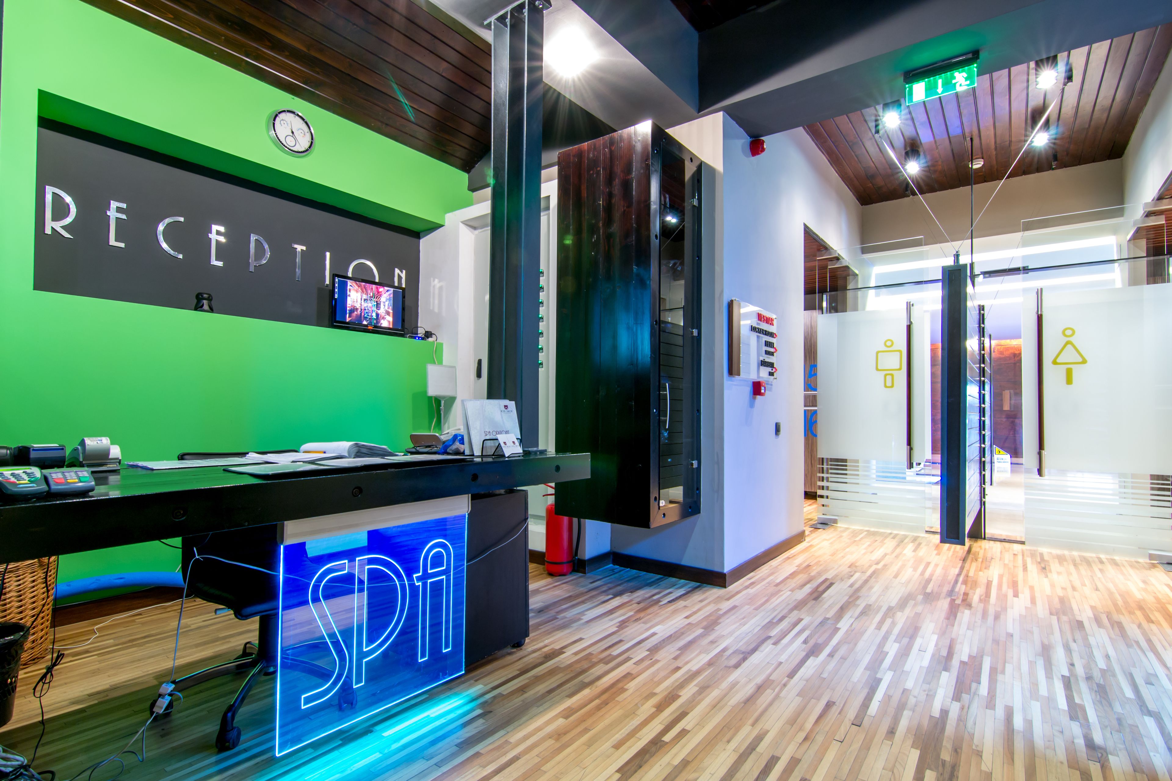 A reception area with a green wall, a neon sign, and a wooden floor.