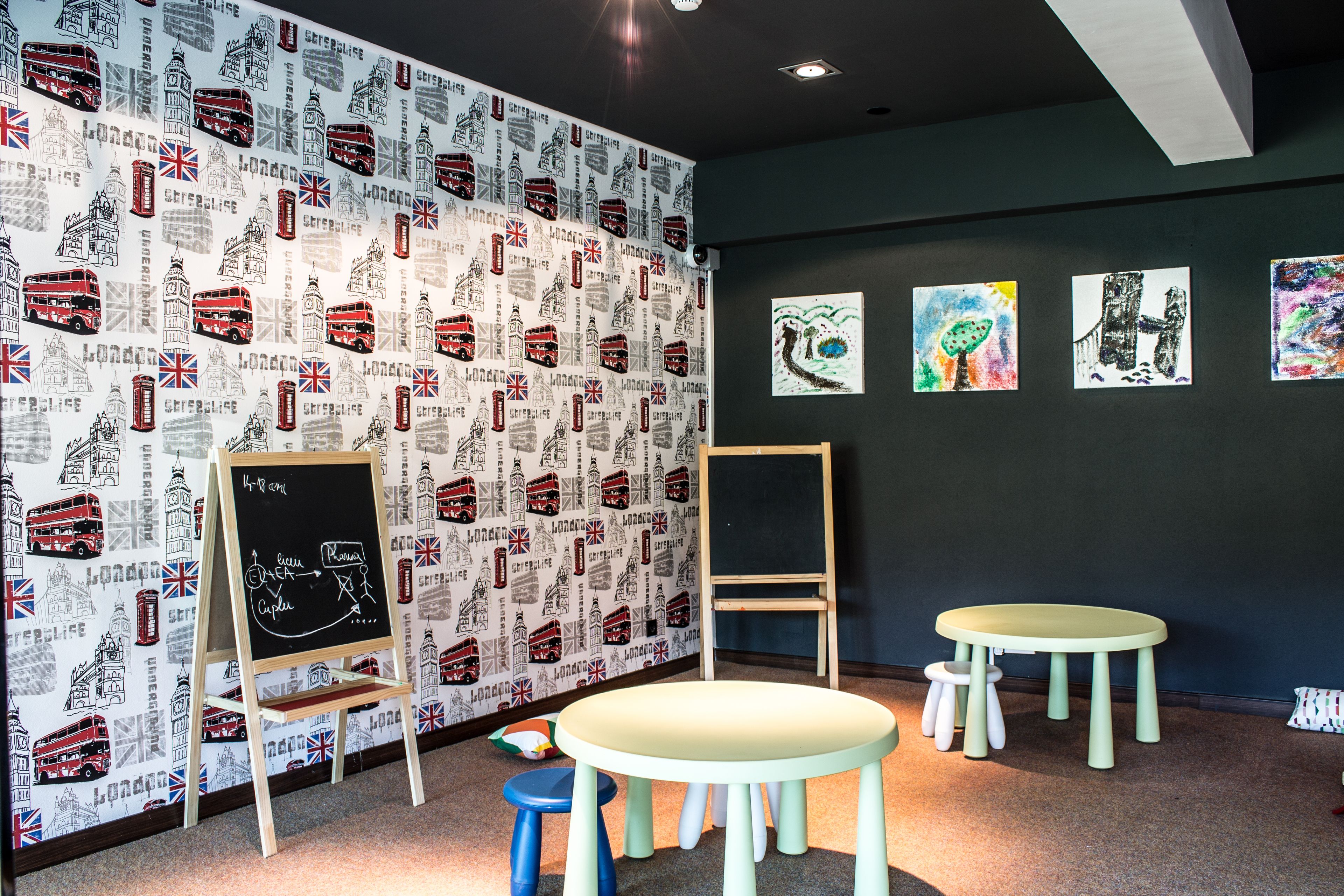 A room with a patterned wallpaper, a chalkboard, a wooden easel, and a small table with stools.