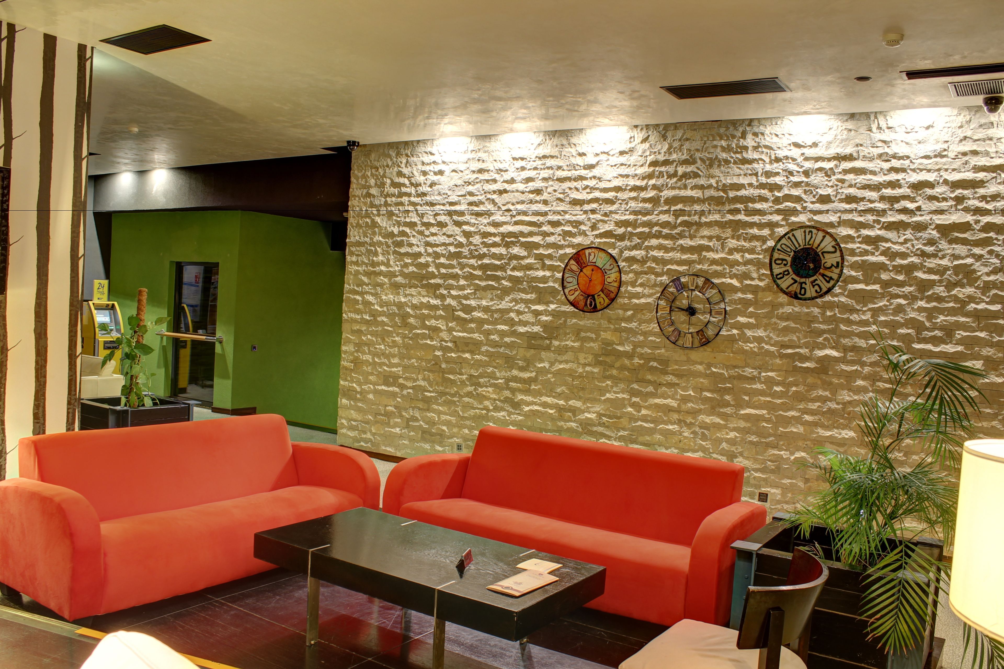 A lobby with a textured stone wall, two clocks, a red sofa, a coffee table, and a plant.