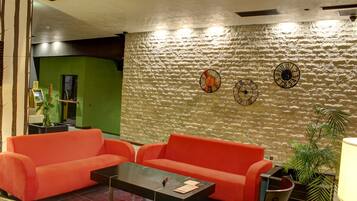 A lobby with a textured stone wall, two clocks, a red sofa, a coffee table, and a plant.