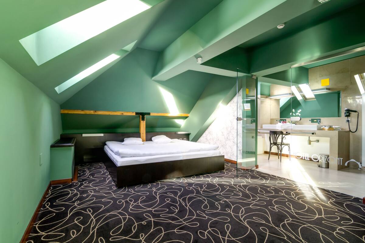 Ein modernes Zimmer mit Schräge, einem Bett, einer kleinen Küchenzeile und einem Badezimmer.