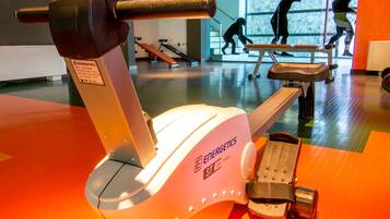 Ein stationäres Fahrrad mit digitaler Anzeige in einem Fitnessstudio mit orangefarbenem Boden und Spiegelwänden.