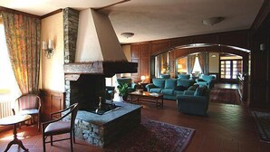 A cozy living room with a stone fireplace, comfortable seating, and a view into the dining area. - Hotel Panoramique (Sarre)