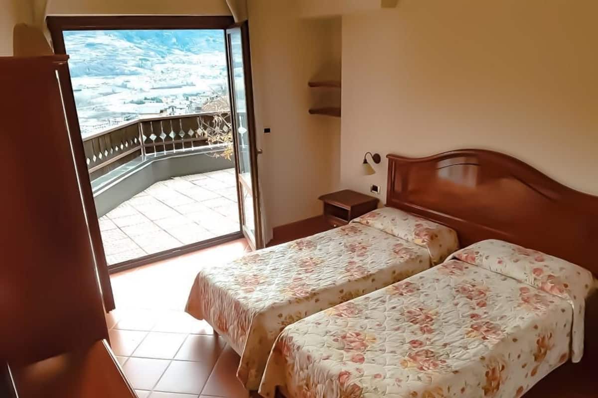 Una habitación con dos camas, una mesita de noche, una pequeña mesa y un balcón con vistas.