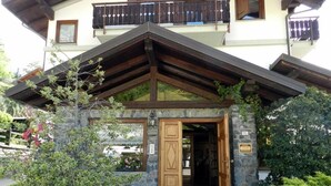 A mountain lodge entrance with a stone facade, wooden doors, and a balcony with a wooden railing. - Hotel Panoramique (Sarre)