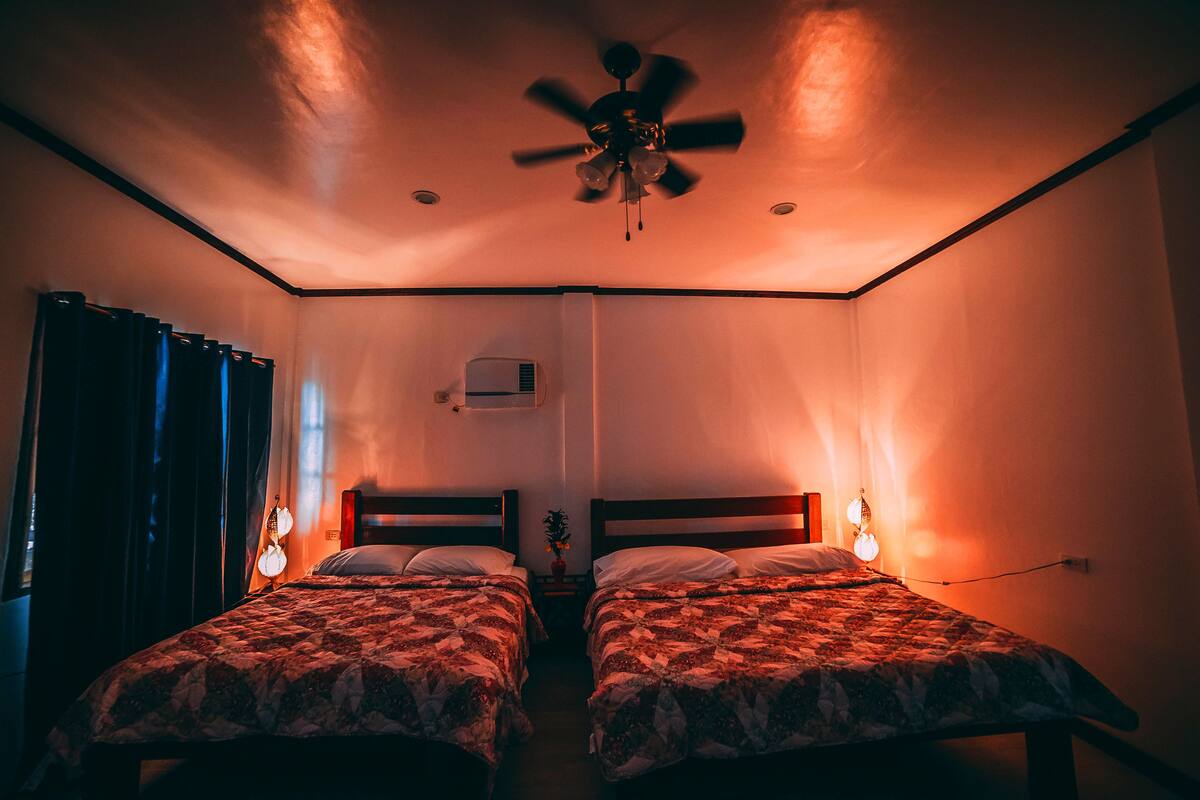 Een kamer met twee bedden, een plafondventilator en een luchtverkoeler aan de muur.