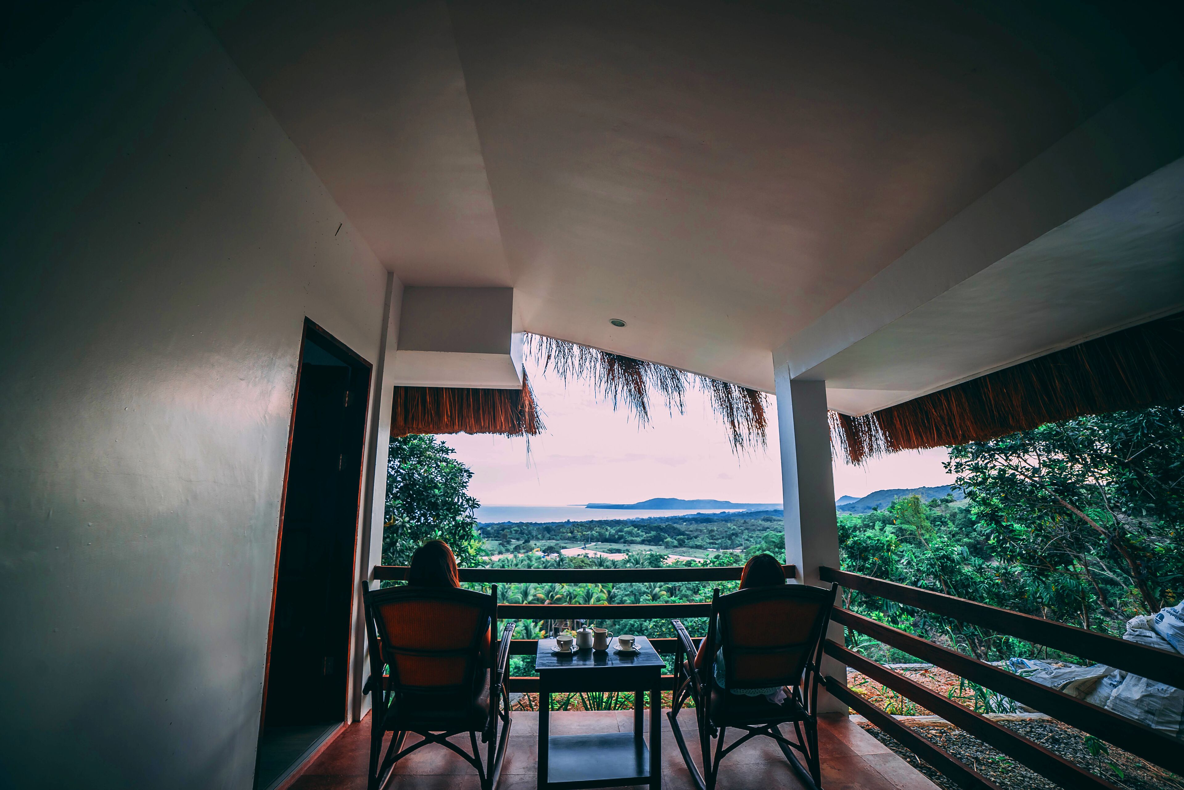 Un balcón con mesa y sillas, con vistas a un paisaje exuberante con árboles y colinas.