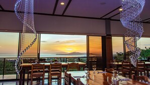 Un restaurante con vista al atardecer, ventanas amplias y decoraciones de cristal colgantes.