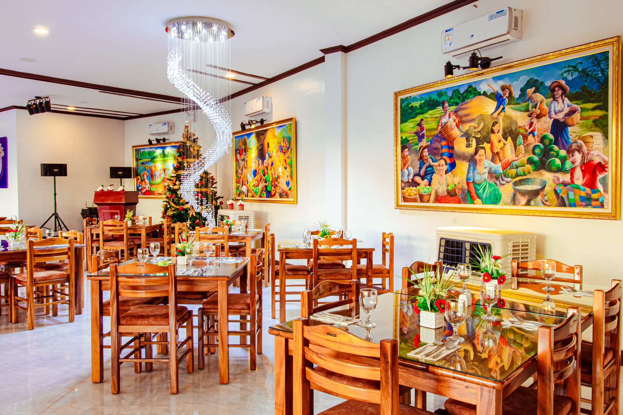 A dining area with wooden tables and chairs, a chandelier, and large paintings on the walls.